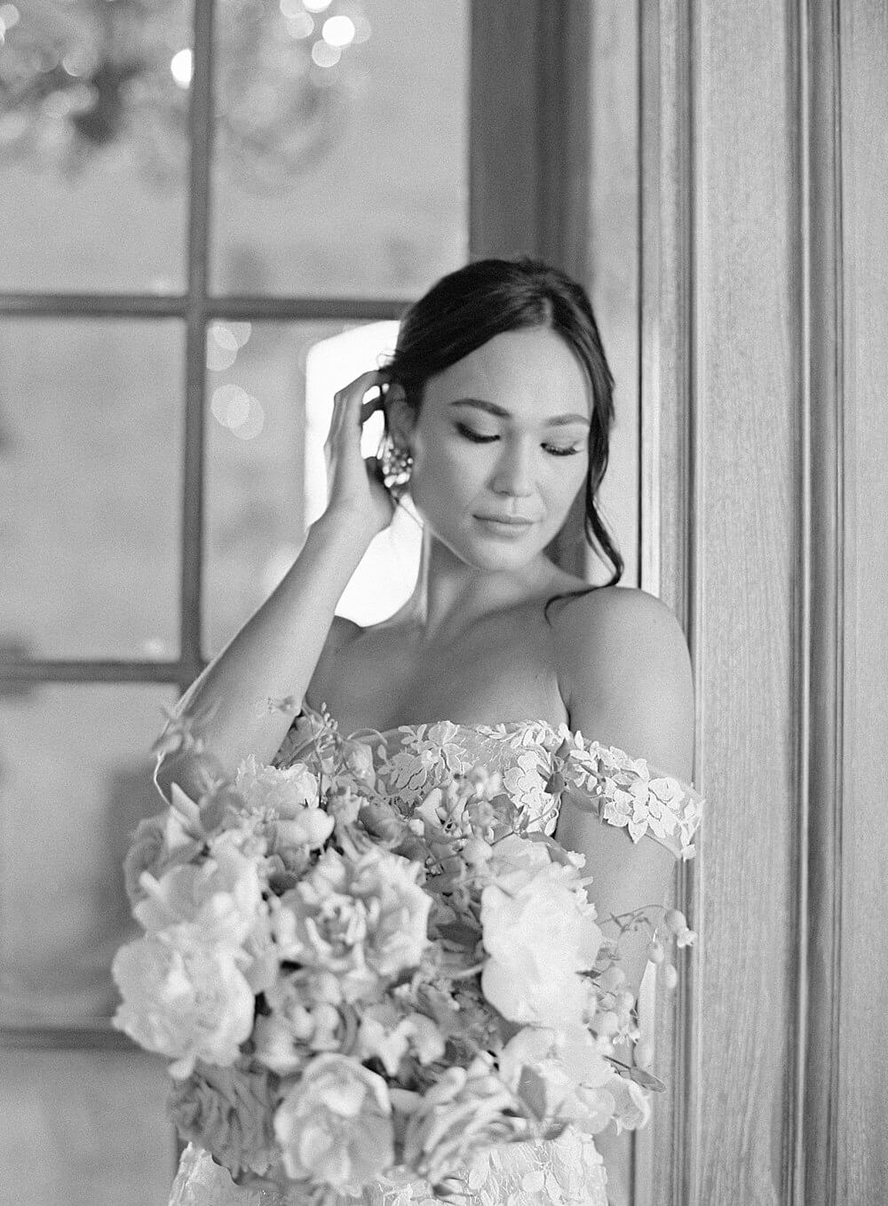 black and white image of bride touching her hair as she looks at her bridal bouquet at cal-a-vie spa - Jacqueline Benét