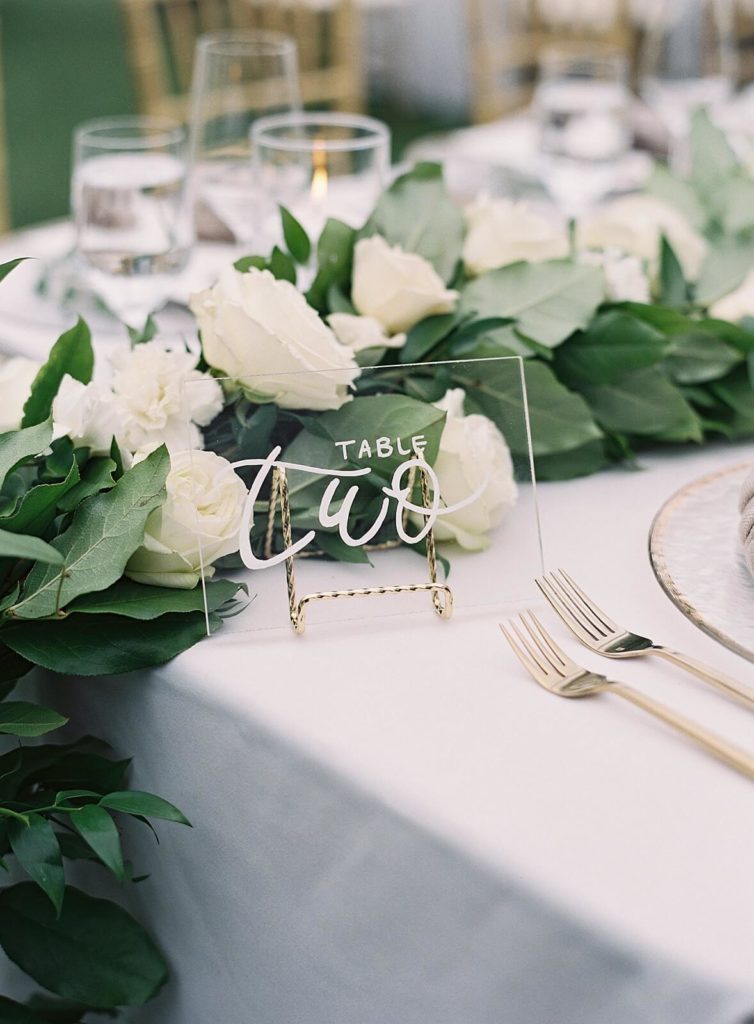 Clear acrylic table number with white calligraphy with gold flatware and white florals at wedding reception - Jacqueline Benét Photography