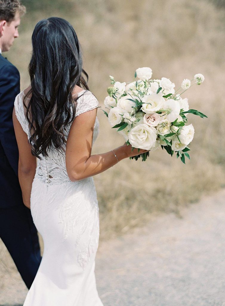 White bridal bouquet in the sun held by bride while walking  - Jacqueline Benét Photography