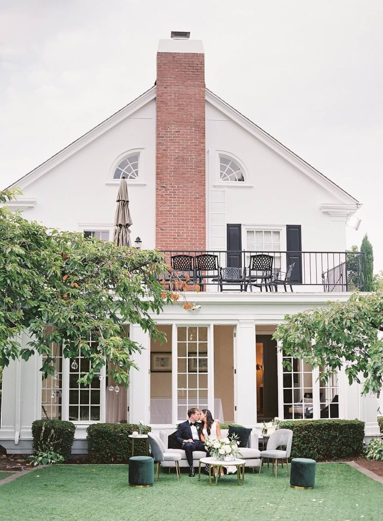 White historic mansion called The Admiral's House with couple kissing while sitting on lounge furniture at Seattle wedding photographed by Jacqueline Benét Photography