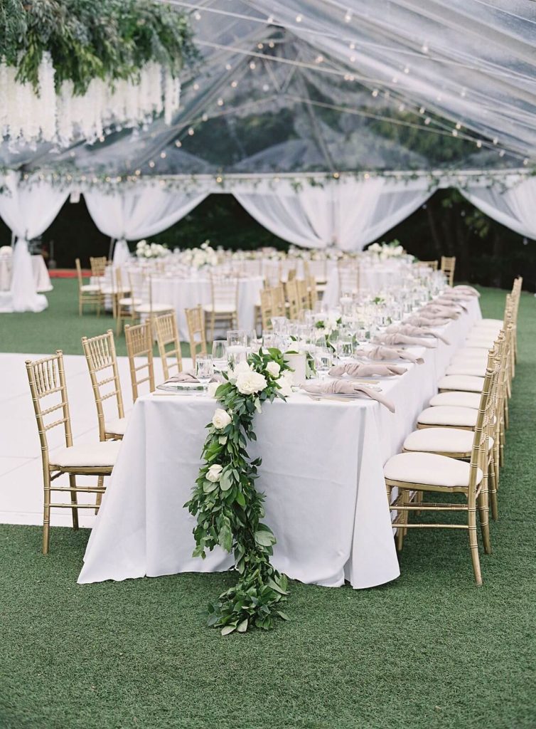 Admirals House wedding reception with white floral and green garland and gold chivari chairs under clear tent - Jacqueline Benét Photography