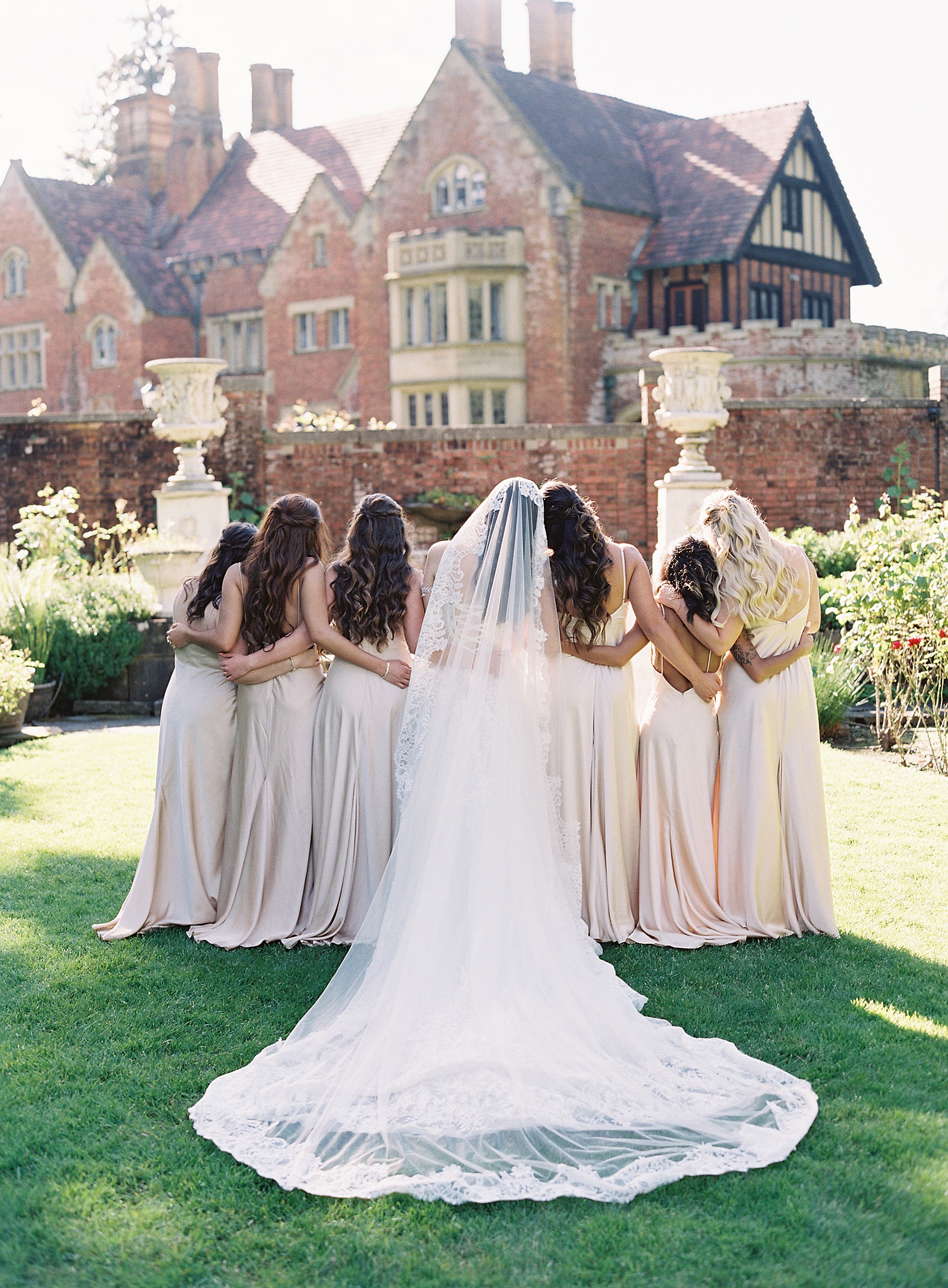 Bride and bridemaids facing toward Thornewood Castle with long lace veil and champagne gowns - Jacqueline Benét Photography
