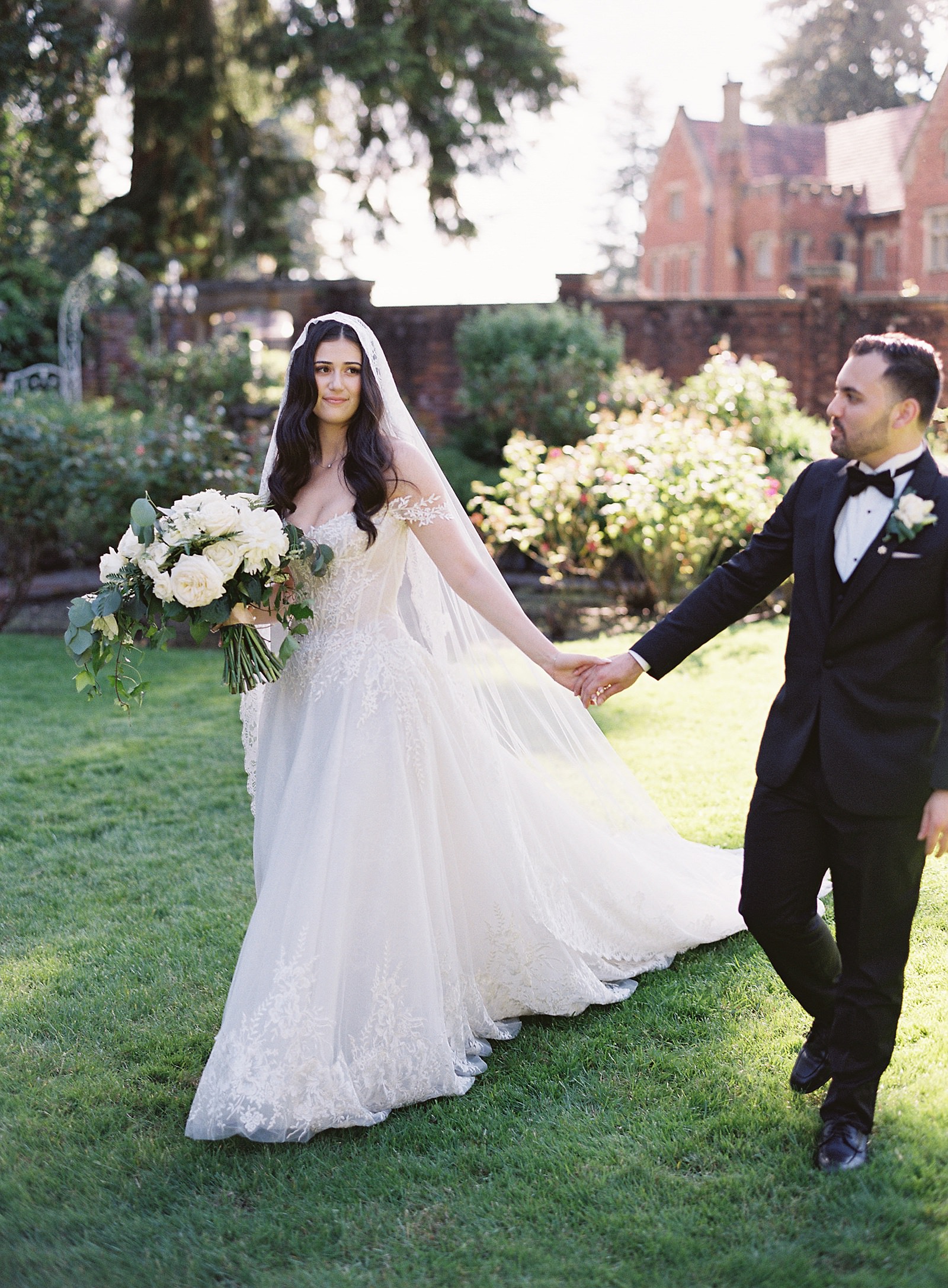 Bride and groom walk in garden in front of Thornewood Castle. Bride wears ines di santo gown and mantilla veil - Jacqueline Benét Photography