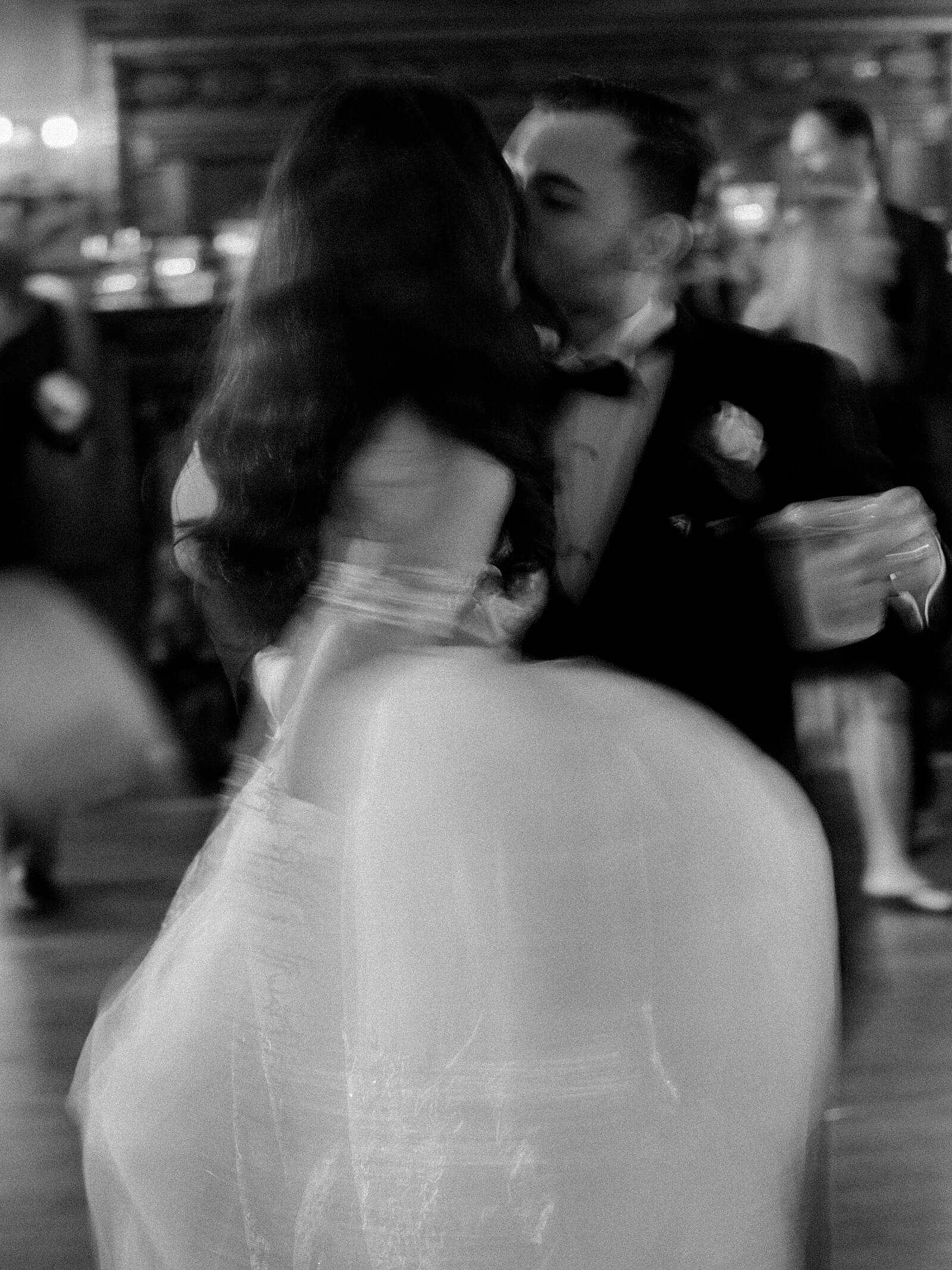 Bride and groom kiss in black and white motion blur photo at their wedding reception - Jacqueline Benét Photography