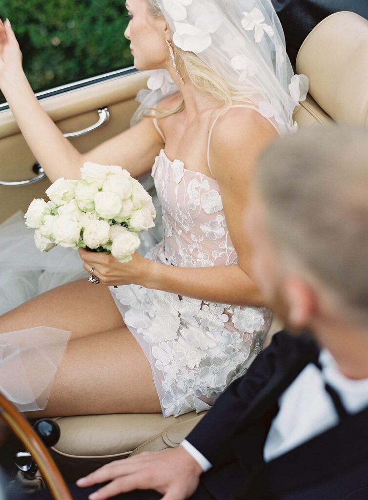 Bride and groom getaway in convertible with close up on little white dress and white roses with Jacqueline Benét Photography