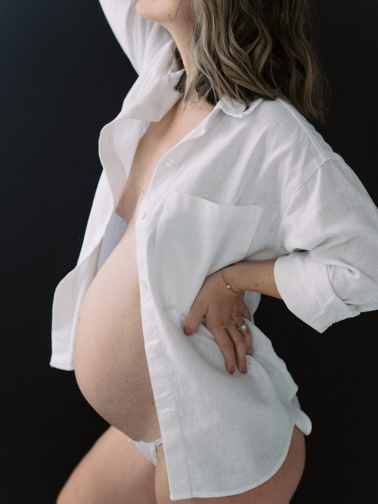 Maternity Photo in Seattle studio with pregnant woman in white button down shirt against a black backdrop