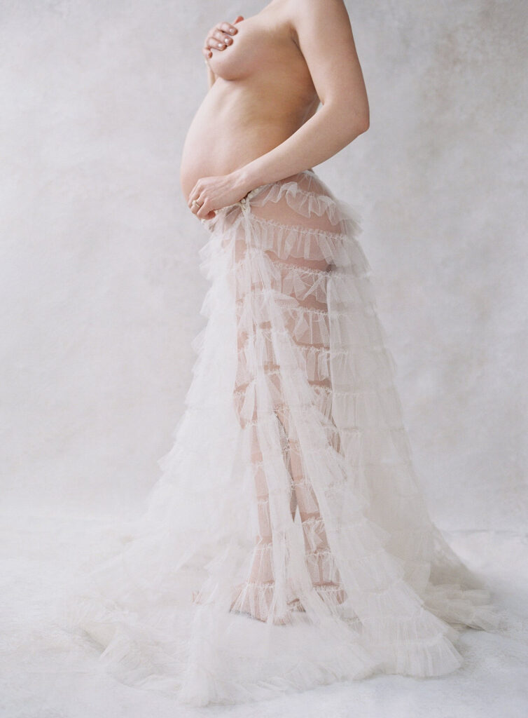 woman showing pregnant belly with sheer tulle skirt in maternity boudoir photoshoot in Seattle