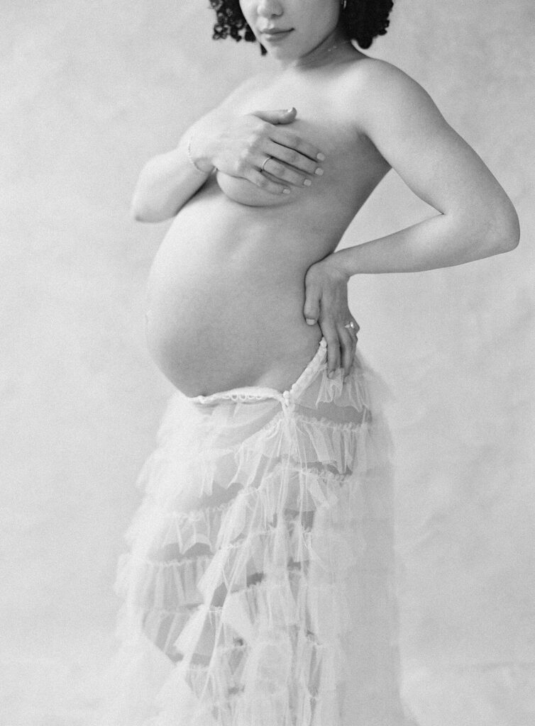 woman in black and white image showing pregnant belly with sheer tulle skirt in maternity boudoir photoshoot in Seattle