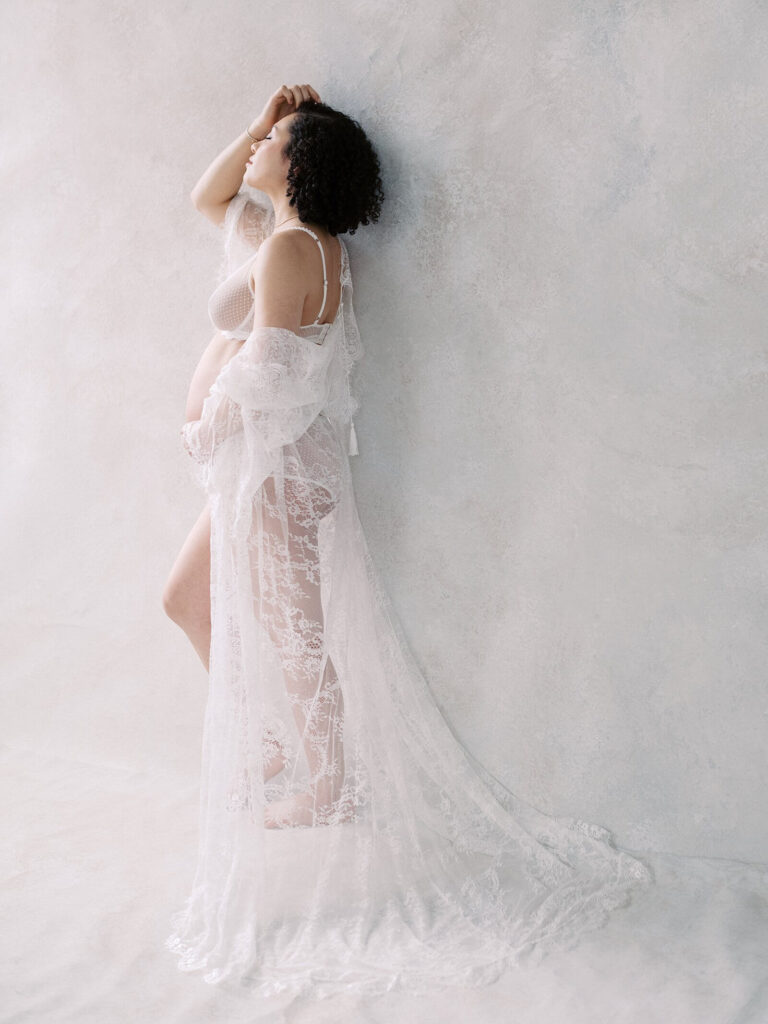 woman in white lacy robe showing pregnant belly in maternity boudoir photoshoot in Seattle