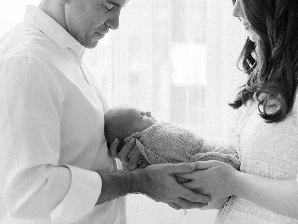 mom and dad smile at newborn baby wrapped in swaddle taken by studio newborn photographer in Seattle Jacqueline Benét