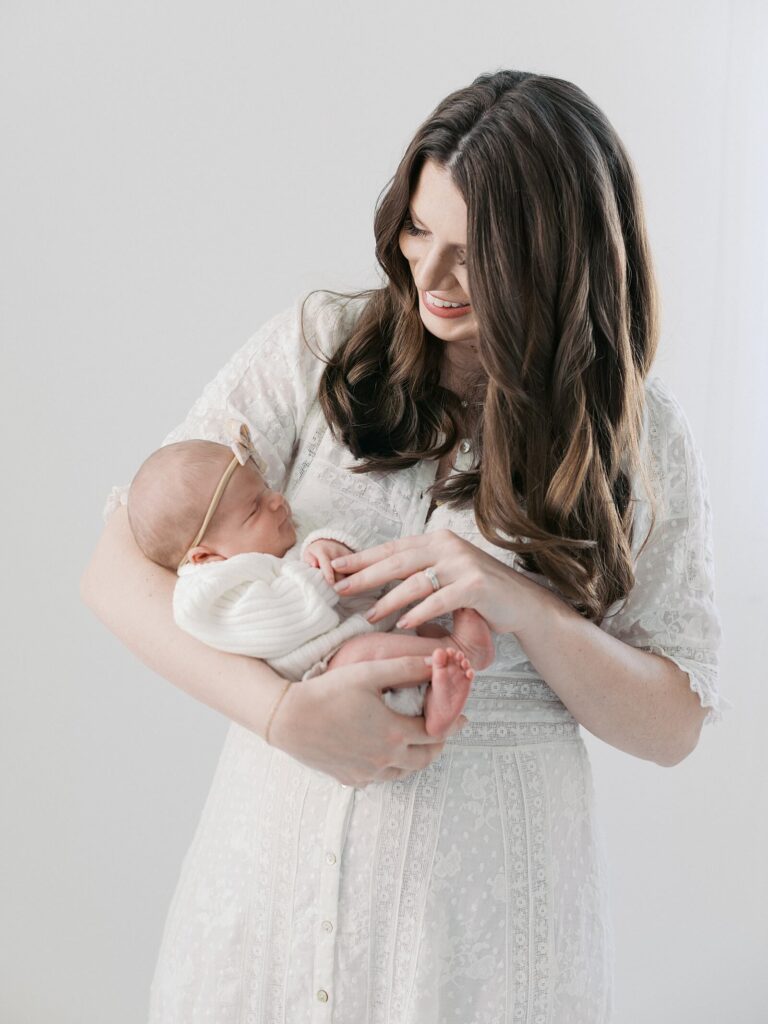 mom smiles down at newborn baby in white sweater outfit in photo taken by Seattle studio newborn photographer Jacqueline Benét
