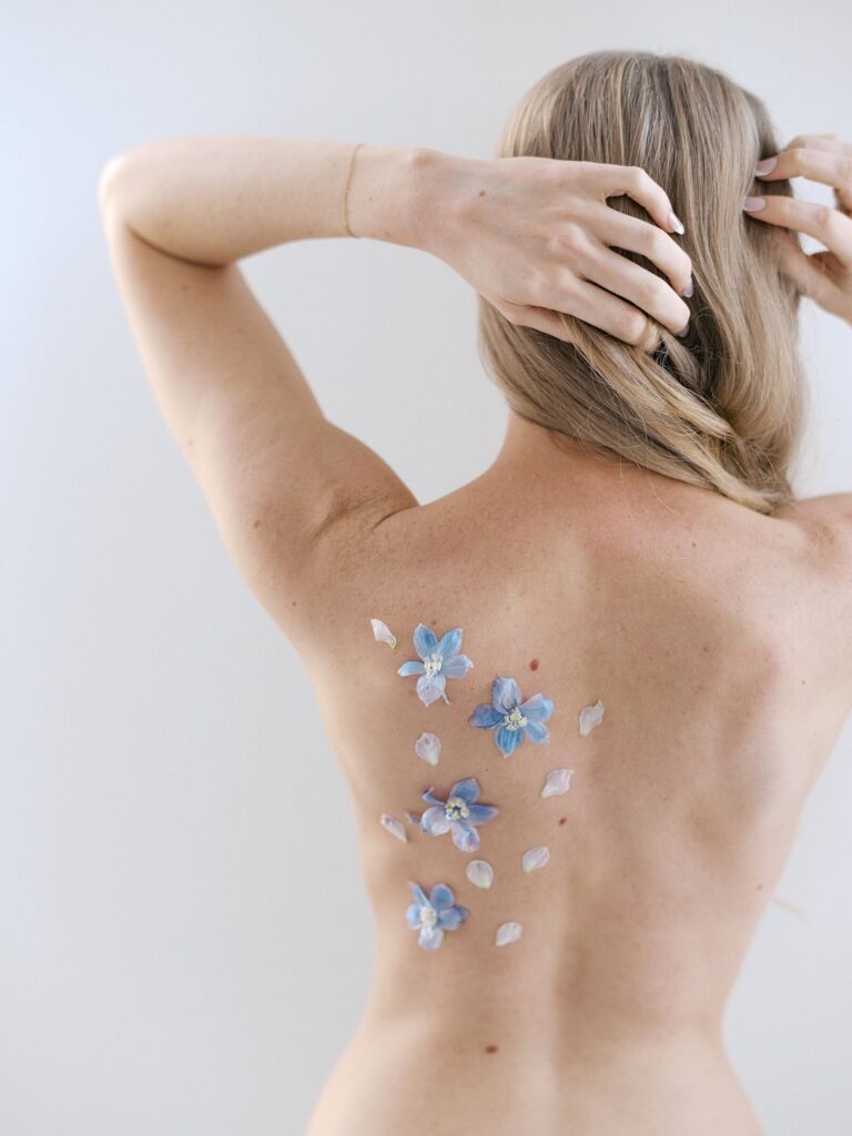 Close-up of a woman’s bare back adorned with pressed blue flowers and petals, captured during a creative birthday boudoir photoshoot.