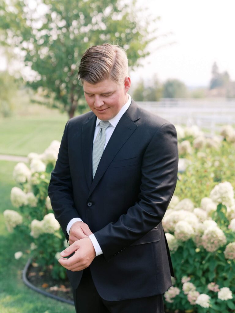 Groom adjusting his cufflinks in a garden surrounded by white hydrangeas before the ceremony at his Harmony Meadows wedding.