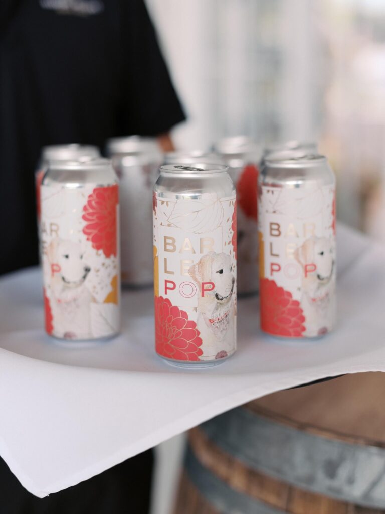 Custom beer cans featuring a floral design and a dog illustration, served on a tray at a Harmony Meadows wedding.