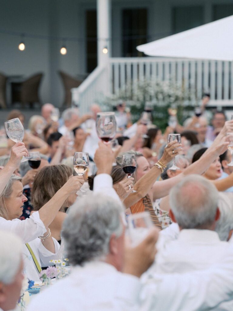 Wedding guests raising their glasses in a celebratory toast during an outdoor reception at a Harmony Meadows wedding.