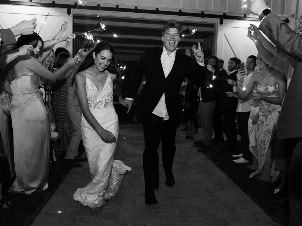 Black and white photo of bride and groom laughing as they run through a sparkler exit at their Harmony Meadows wedding.