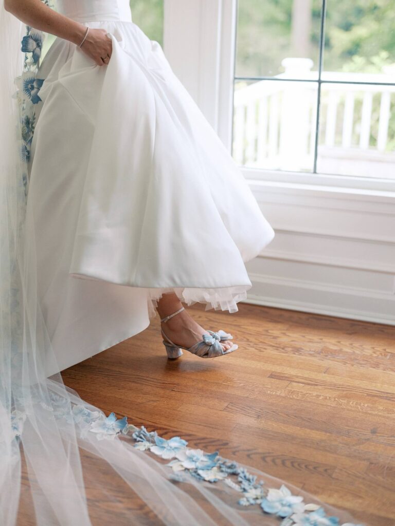 A close up of the brides classic white wedding dress and pastel blue and white heels as she prepares for her garden wedding at Fox Hollow Farm in Seattle. Captured by Jacqueline Benét - Seattle wedding photography