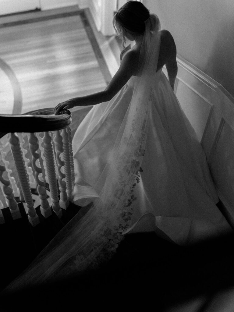 The bride walking down the front stairway with her long train trailing behind her at Fox Hollow Farm - one of the top garden wedding venues in Seattle - by Jacqueline Benét 