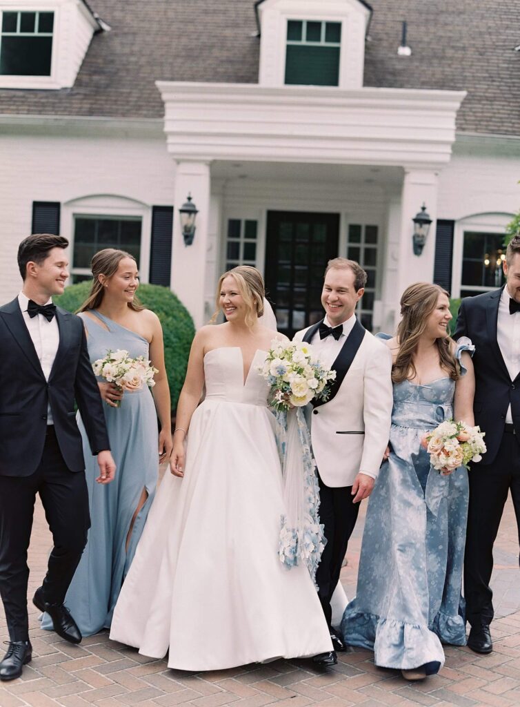 Bridesmaids gathered around the bride in soft pastel dresses and groomsmen in black tuxedos, laughing together in the gardens at Fox Hollow Farm, photographed by Jacqueline Benét | Seattle wedding photography