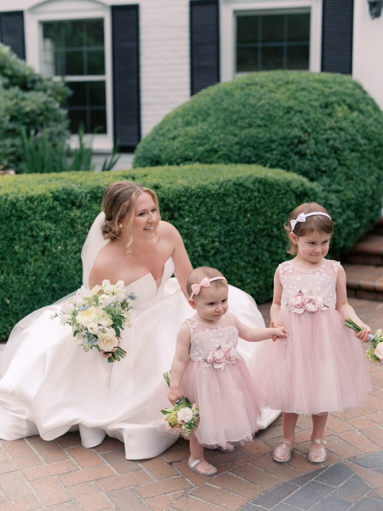 The bride squatting down to take a photo with the sweet flower girls as they prepare for the garden ceremony on the estate ground of Fox Hollow Farm, photographed by Jaqueline Benét | Seattle wedding photographer