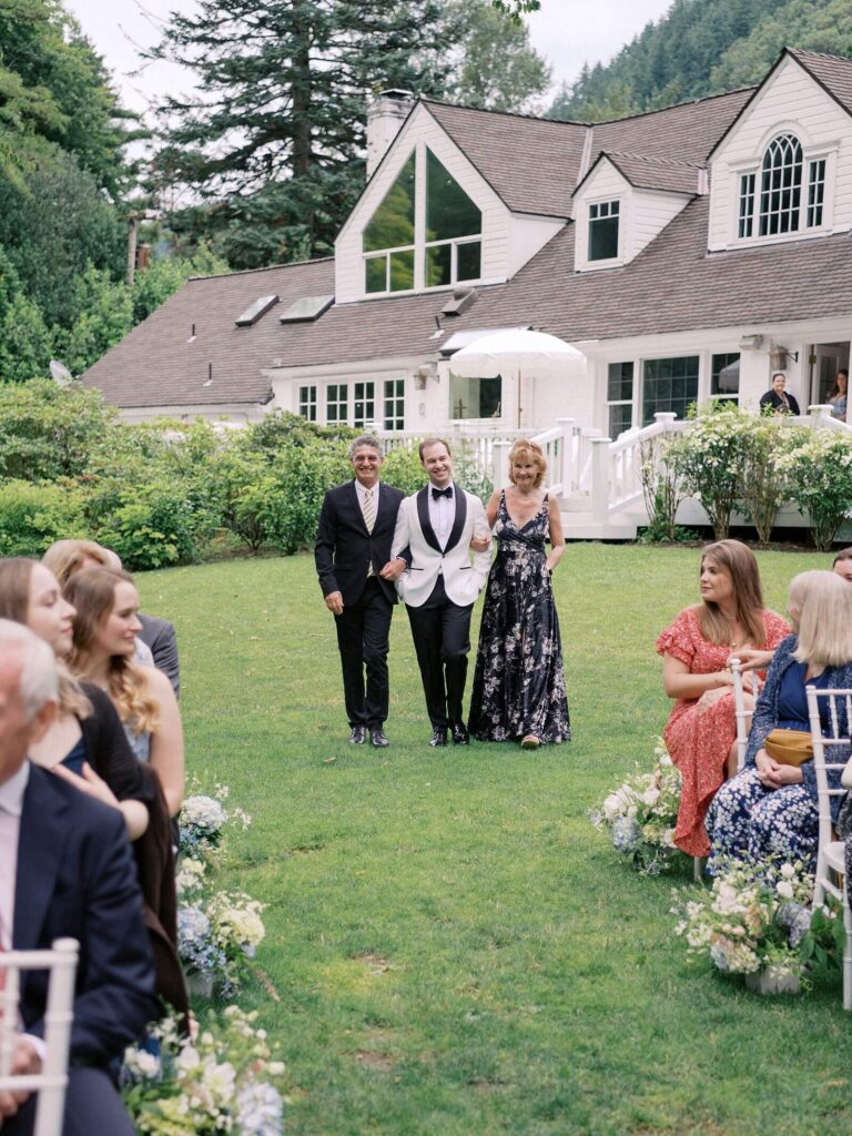 The groom being escorted down the isle by his parents, smiling to the wedding guests. Photographed by Jacqueline Benét, Seattle Wedding Photographer 