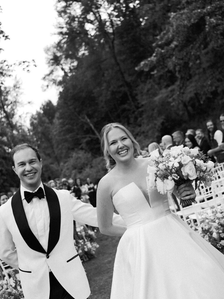 A classic black and white photo of the bride and groom walking down the isle together and smiling with such joy after saying "i do". Captured by Jacqueline Benét - Seattle wedding photography