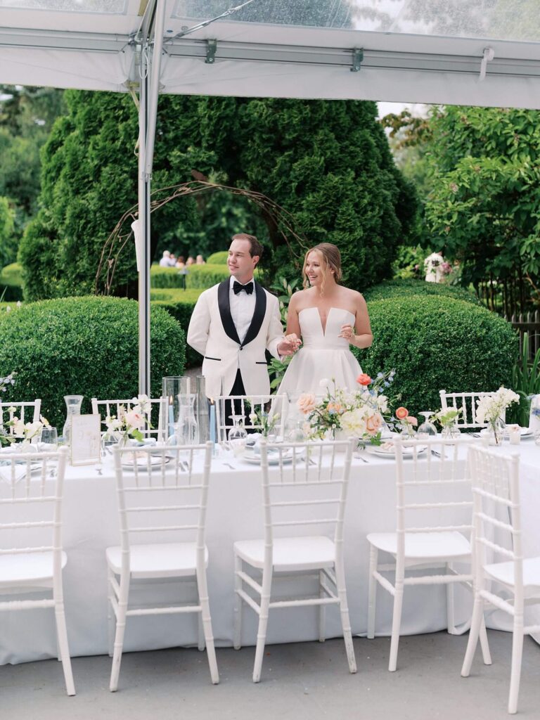 The bride and groom standing under the reception tent look around at the beautiful decor of their reception tables at their fox hollow farm wedding in Seattle - photo by Jacqueline Benét 