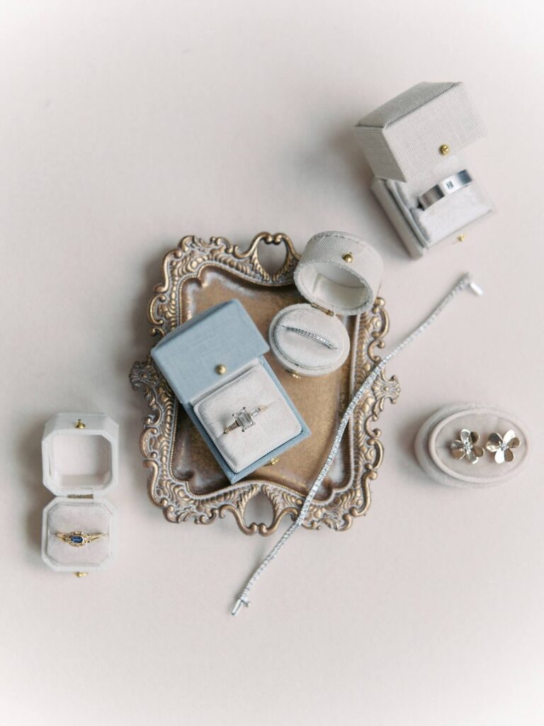 wedding rings displayed on an antique tray with small ring boxes and a tennis bracelet