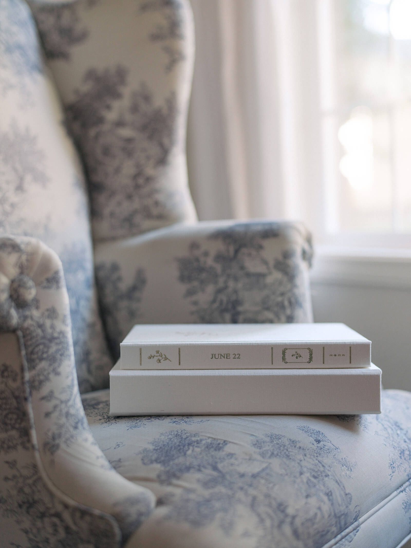 A linen covered heirloom wedding album sitting in a wingback chair.